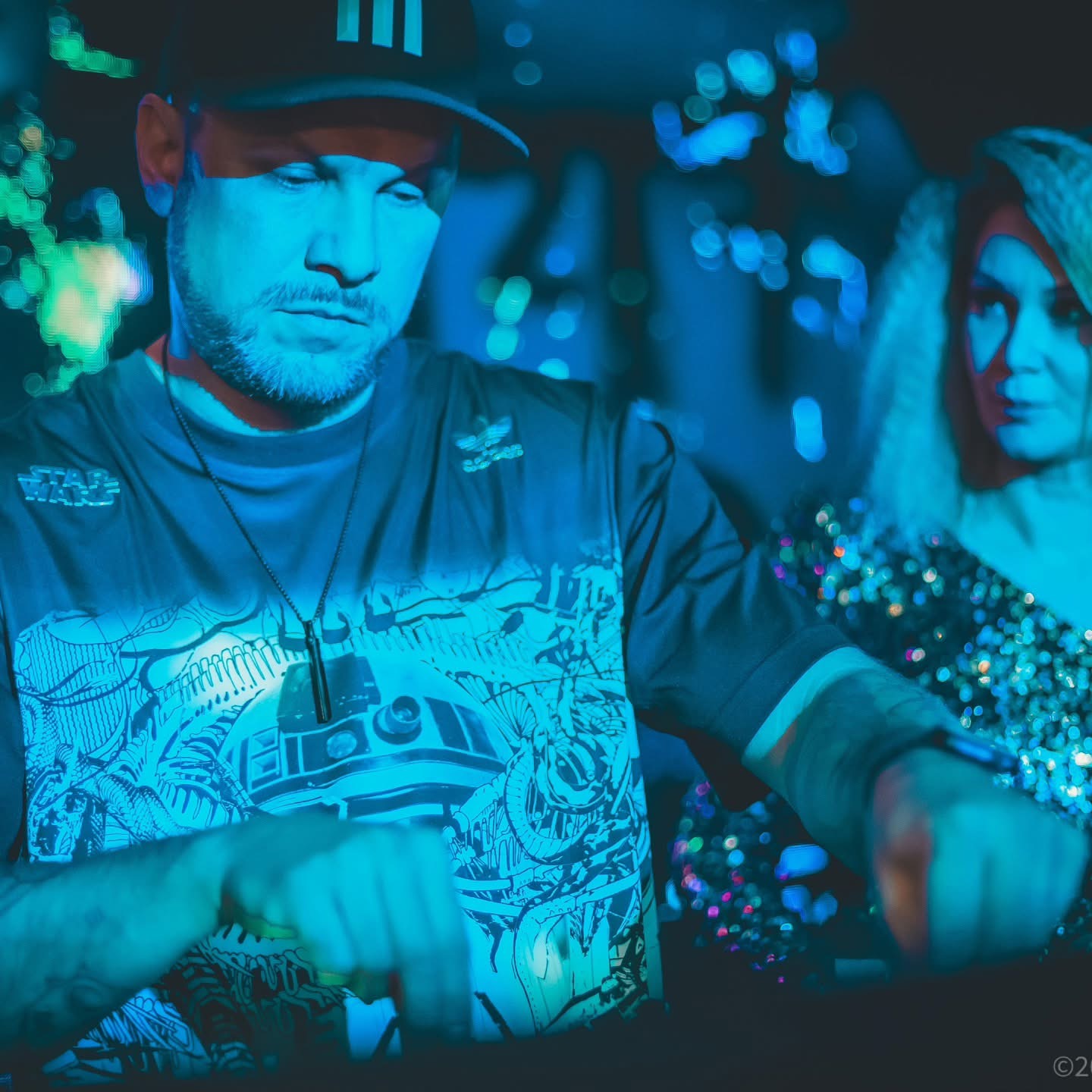 Y:I behind the booth bathed in cyan club light